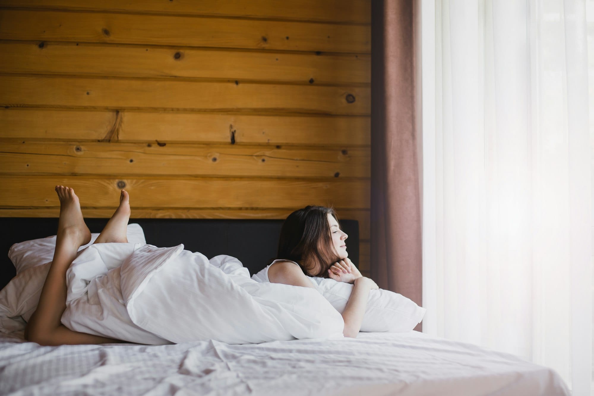 Woman relaxing in bed near window in cozy log cabin or wooden house